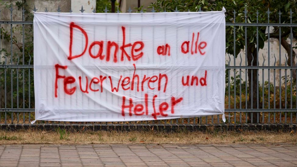 Ein Transparent mit der Aufschrift «Danke an alle Feuerwehren und Helfer» hängt an einem Zaun. (Quelle: dpa/Jan Woitas)