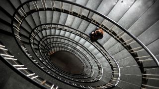 Symbolbild: Eine Frau steht in einem sprialenförmigen Treppenhaus. (Quelle: dpa/J. Stratenschulte)