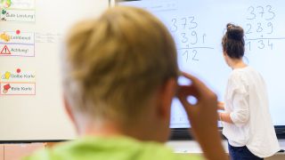 Symbolbild: Ein Lehrerin schreibt eine Mathematikaufgabe auf eine digitale Schultafel im Klassenraum einer 4. Klasse einer Grundschule. (Quelle: dpa/Stratenschulte)
