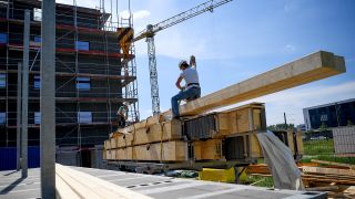 Archivbild: Ein Arbeiter hängt am 24.05.2018 einen Holzbalken an einen Kran auf einer Baustelle der Wohnungsbaugesellschaft Howoge. (Quelle: dpa/Britta Pedersen)