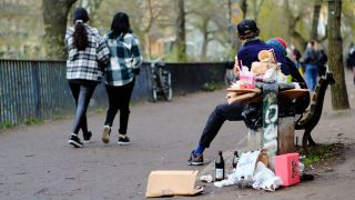 Abfall liegt neben einem Ã¼berfÃ¼llten MÃ¼lleimer am Planufer im Stadtteil Kreuzberg am Wegesrand neben einer Bank, auf der Menschen sitzen.