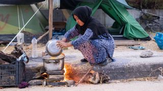 Arhivbild: Eine GeflÃ¼chtete kocht am Boden Ã¼ber einem Feuer Essen in einem FlÃ¼chtlingscamp auf Lesbos. (Bild: picture alliance / NurPhoto)