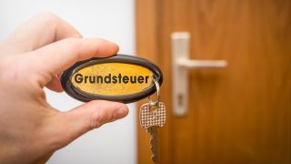 Mann hÃ¤lt SchlÃ¼ssel der HaustÃ¼re in der Hand mit der Aufschrift: Grundsteuer (Bild: picture alliance) 