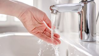 Eine Frau lässt Wasser aus einem Wasserhahn über ihre Hand fließen.