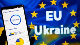 Vor einer Flagge, die die EU und die Ukraine symbolisiert, ist eine Grafik mit den bisherigen Zahlungen an das Land abgebildet (Bild: picture alliance/ NurPhoto) 