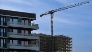 Ein BaugerÃ¼st steht an der Fassade von einem nicht fertig gebauten BÃ¼rohaus auf einer Baustelle im Zentrum der Stadt. Im Vordergrund ist ein neugebautes Wohnhaus zu sehen.