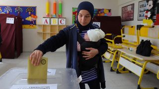 Eine Frau mit einem Baby auf dem Arm wirft ihren Stimmzettel in einem Wahllokal in Ankara in eine Wahlurne. 