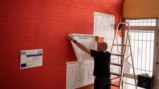 Ein Mitarbeiter hÃ¤ngt Kandidaten- und Parteilisten an die Wand eines Wahllokals in Griechenland.