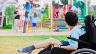 Ein Junge im Rollstuhl schaut anderen Kindern auf dem Spielplatz zu