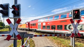 Eine Schranke ist an einem BahnÃ¼bergang in LÃ¼bbenau geschlossen, wÃ¤rend ein Regionalzug vorbeifÃ¤hrt.