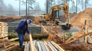 Ein Ã¤lterer Mann steht auf einer Baustelle und hebt Holzbretter an (Bild: Colourbox)