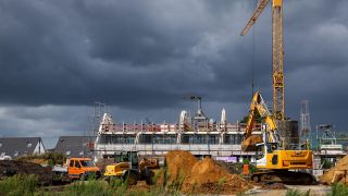 In einem Neubaugebiet stehen KrÃ¤ne und Bagger an einem Wohnungsbauprojekt.