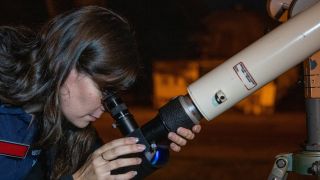 Eine Frau richtet ein Teleskop in den Sternenhimmel.