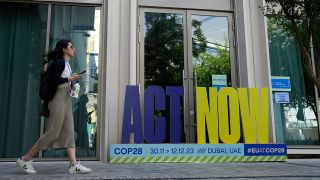 Eine Frau lÃ¤uft an einem Aufsteller der COP28 vorbei, der die Aufschrift 