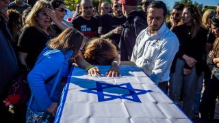 Familie und Freunde trauern wÃ¤hrend einer Beerdigung, auf dem Sarg liegt eine israelische Flagge.