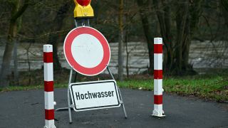 Ein Schild warnt an einem gesperrten Weg vor dem Hochwasser. 