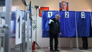 Ein Mann kommt aus einer Wahlkabine. Ãber den Kabinen hÃ¤ngt ein PortrÃ¤t von Wladimir Putin. 