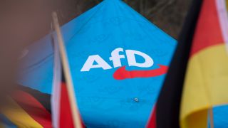 Das Logo der AfD ist bei einer Kundgebung in DÃ¼sseldorf neben Deutschlandflaggen auf einem Zeltpavillion zu sehen.