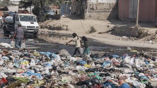 Zwei MÃ¤dchen tragen in Dair El balah Wasserkanister Ã¼ber eine mit MÃ¼lltÃ¼ten verunreinigte StraÃe. 