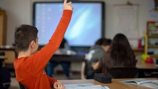 Ein SchÃ¼ler meldet sich wÃ¤hrend des Unterrichts in einer Grundschule mit Handzeichen.