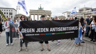 Teilnehmende einer Demonstration halten vor dem Brandenburger Tor ein Banner mit der Aufschrift 