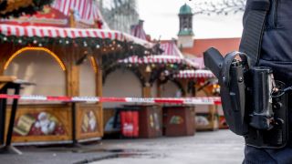 Eine Schusswaffe am GÃ¼rtel eines Polizeibeamten, im Hintergrund ist ein Absperrband und der Magdeburger Weihnachtsmarkt zu sehen.