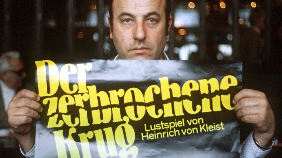 Der Schauspieler Manfred Krug hält im Januar 1985 anlässlich einer Tournee mit dem Lustspiel "Der zerbrochene Krug" ein Werbeplakat in den Händen; © picture-alliance/dpa/Werner Baum