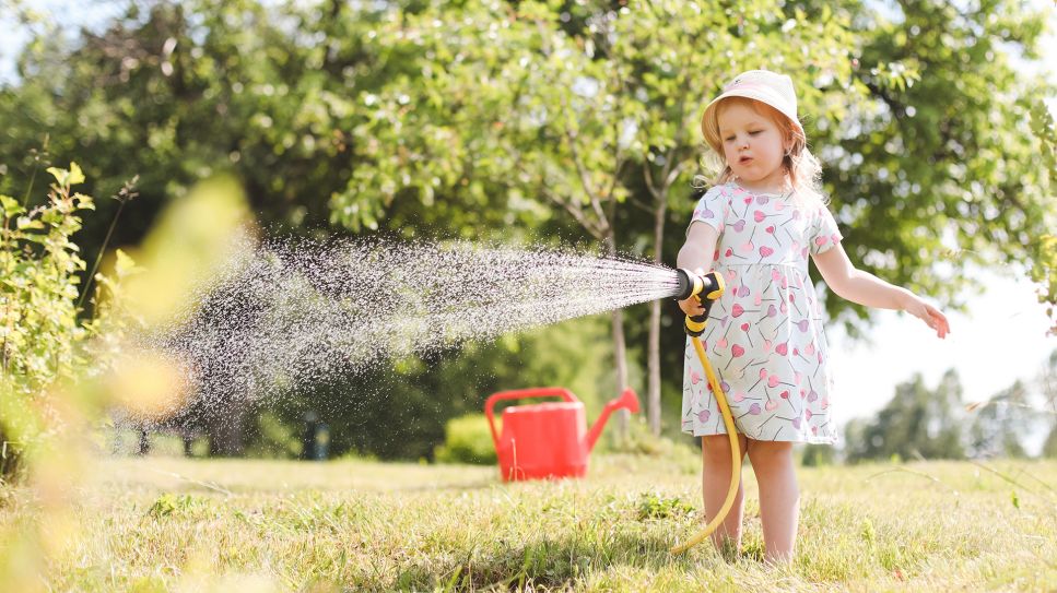 Kleines Mädchen mit Sommerhut gießt mit einem Wasserschlauch den Garten (Bild: Colourbox)