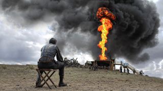 Daniel Plainview (Daniel Day-Lewis) schaut ölgetränkt sitzen auf Rauch- und Feuersäulesäule