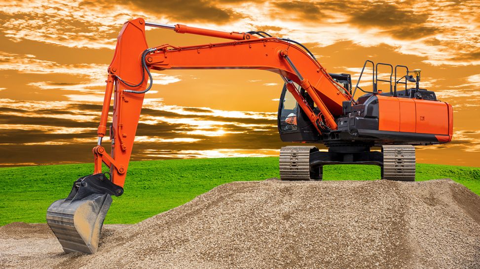 Bagger auf Kieshaufen vor grüner Wiese (Bild: Colourbox)