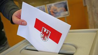Symbolbild:Ein Wähler wirft einen Umschlag mit einem Brandenburg-Wappen in eine Wahlurne.(Quelle/picture alliance/U.Baumgarten)